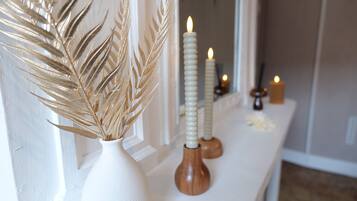 Un jarrón blanco con espigas de trigo seco, dos velas con bases de madera y una vela pequeña sobre una mesa en una habitación con una puerta blanca y un espejo.