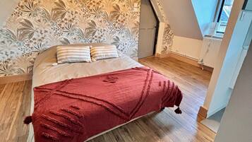 Une chambre avec un plancher en bois, un lit recouvert d’une couverture rouge et un mur décoratif orné de motifs floraux.