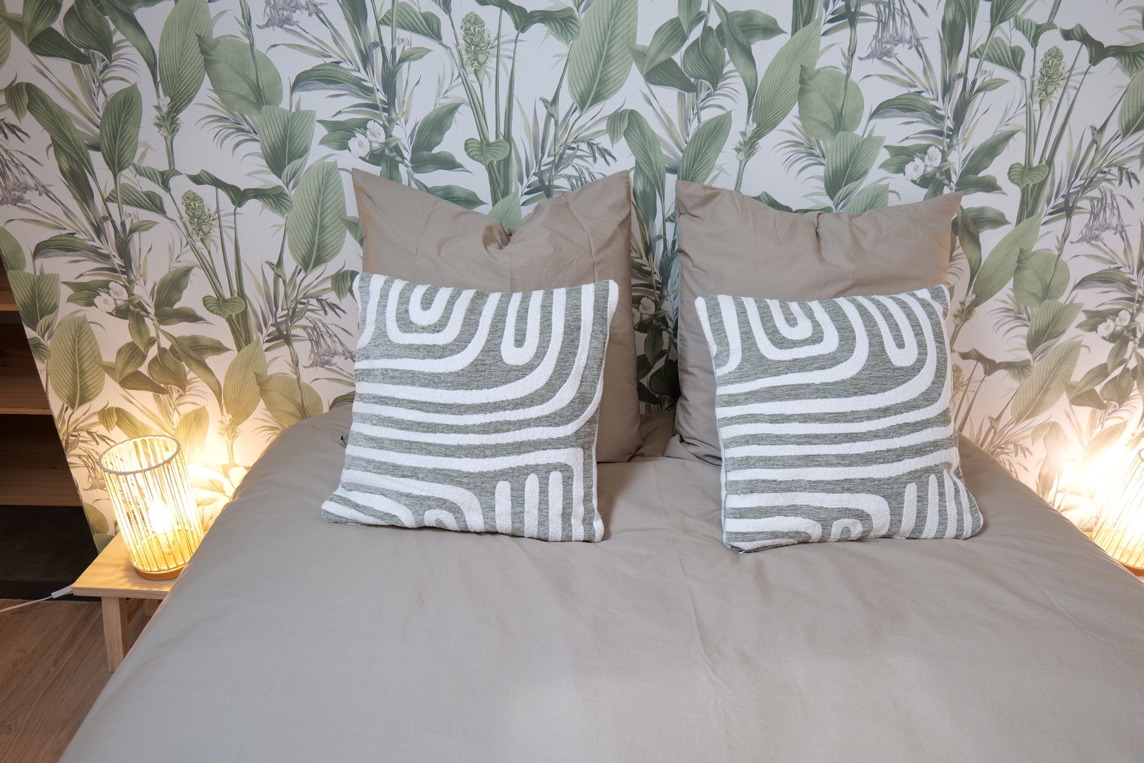 Una cama con dos almohadas, una lámpara de noche y un fondo de papel tapiz floral.