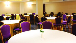 Une salle de conférence dotée de tables rondes et de chaises violettes, équipée de luminaires au plafond et d’un pilier central.