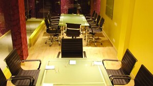 Une salle de conférence avec une table en verre, des chaises noires et des murs jaunes.