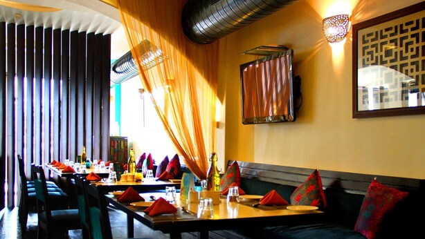 Un restaurant avec une longue table à manger, des chaises et un canapé avec des coussins rouges.