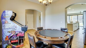 Een eetruimte met een ronde tafel, stoelen, een kroonluchter en een groot arcade spel.
