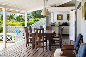Une terrasse en bois avec une table et des chaises, un luminaire suspendu et une vue sur un jardin luxuriant.