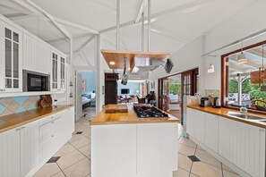 Une cuisine moderne avec des meubles blancs, un plan de travail en bois et un îlot central doté d’une plaque de cuisson.