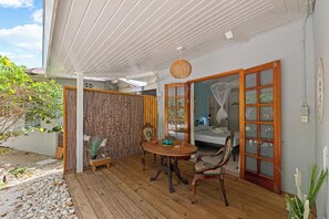 Une terrasse en bois avec une table ronde et des chaises, une clôture en bois et une pièce comprenant un lit et une fenêtre.