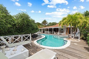 A wooden deck with a swimming pool, surrounded by lush greenery and a covered seating area. - Villa Ranje Louise
Luxury holiday villa for a stylish holiday! (Willemstad)
