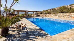 A swimming pool with stone tiles, a pergola, and palm trees. - Aegean Whisper Home (Paros)