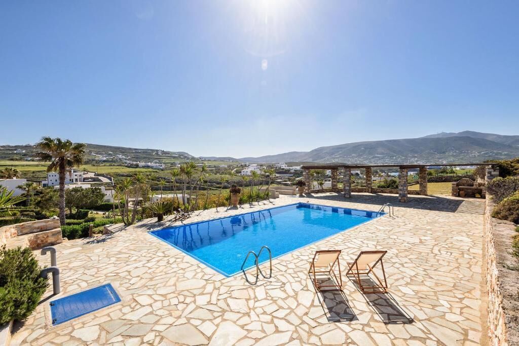 A swimming pool with stone flooring, two lounge chairs, and a pergola.