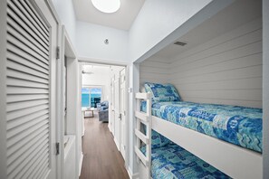 Un couloir étroit mène à une chambre dotée de lits superposés, offrant une vue sur la mer, et une porte avec une fenêtre.