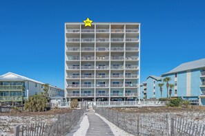A multi-story hotel with a star symbol on the top, balconies, and a pathway leading to the entrance. - New Rental, Direct Beachfront, Top Floor, New Decor, Heated Pool, Kids Bunks (Gulf Shores)