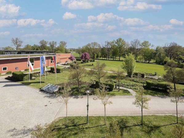 A building with a red facade, a paved courtyard, and a grassy park area with trees and a pathway. - Komfortables Studio am Kurpark in Bad Birnbach (Bad Birnbach)