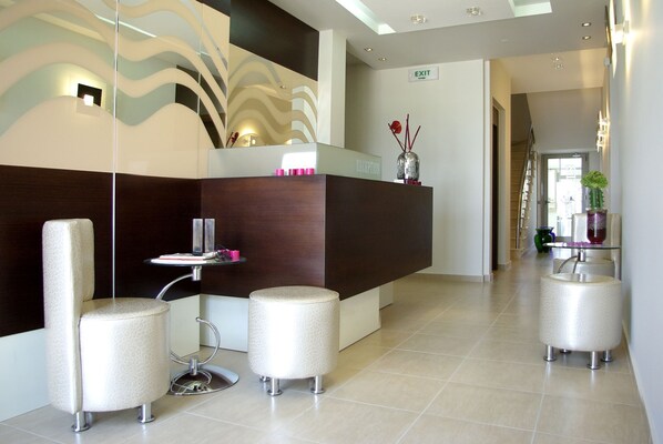 Un área de recepción moderna con un mostrador, dos sillones acolchados, una mesita y un jarrón decorativo.