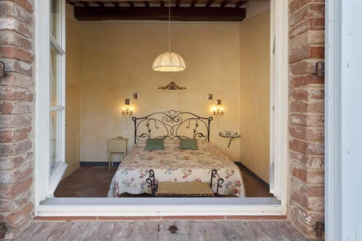 A bedroom with a bed, a nightstand, a hanging light fixture, and a brick wall.
