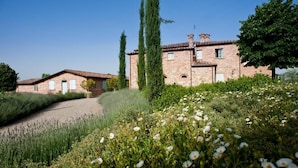 A stone building with a tiled roof, surrounded by a garden with various plants and flowers. - Poggio al Vento Casa Vacanze (Foiano della Chiana)
