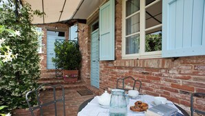 A patio with a table set for tea, a brick wall, and a window with shutters. - Poggio al Vento Casa Vacanze (Foiano della Chiana)