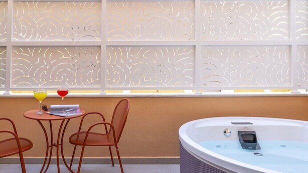 Une pièce avec un jacuzzi, une table et des chaises, ainsi qu’une fenêtre décorative ornée d’un motif.