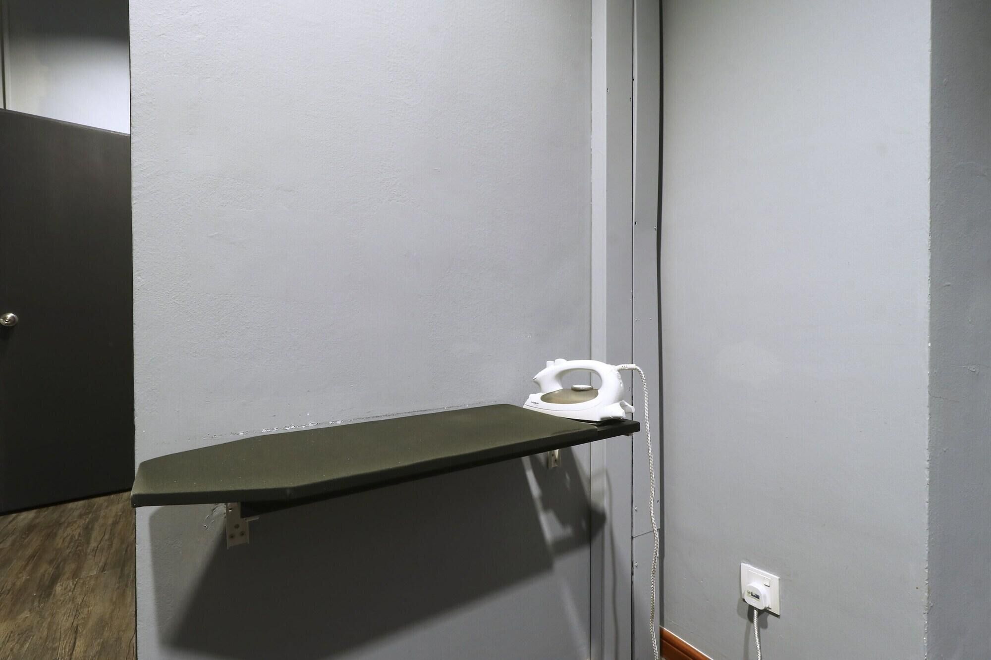 A corner with a grey wall, a black door, and a white electric iron on a black shelf.