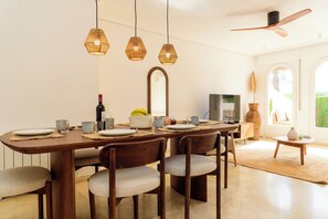 Un comedor con mesa de madera, sillas, luces colgantes, un espejo y un televisor.