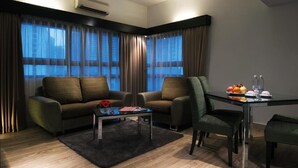 A modern living room with a sofa, armchair, coffee table, and dining table with a fruit bowl. - Crown Regency Serviced Suites (Kuala Lumpur)