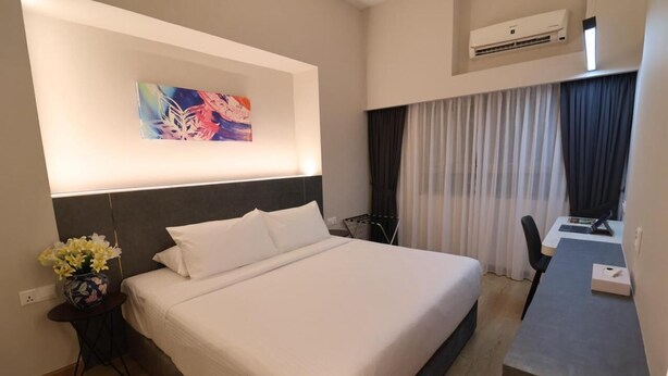A hotel room with a bed, a desk, a chair, a painting on the wall, and an air conditioning unit. - Crown Regency Serviced Suites (Kuala Lumpur)