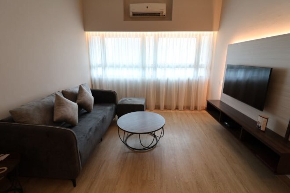 A modern living room with a sofa, a coffee table, a flat-screen TV, and a large window with curtains.