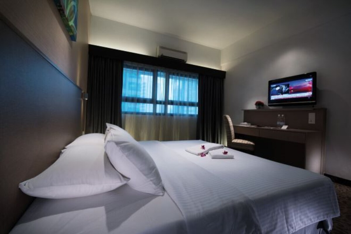 A hotel room with a bed, a television, a desk, and a window with curtains.