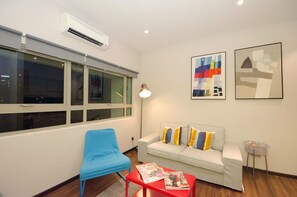 Un salon moderne avec un fauteuil bleu, un canapé blanc agrémenté de coussins colorés et deux œuvres d’art encadrées accrochées au mur.