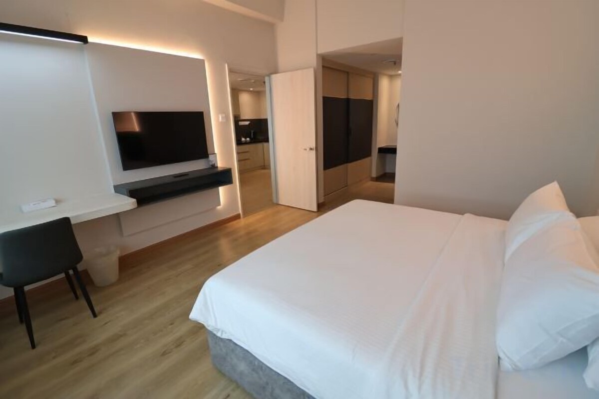 A hotel room with a bed, a desk, a TV, and a kitchenette.