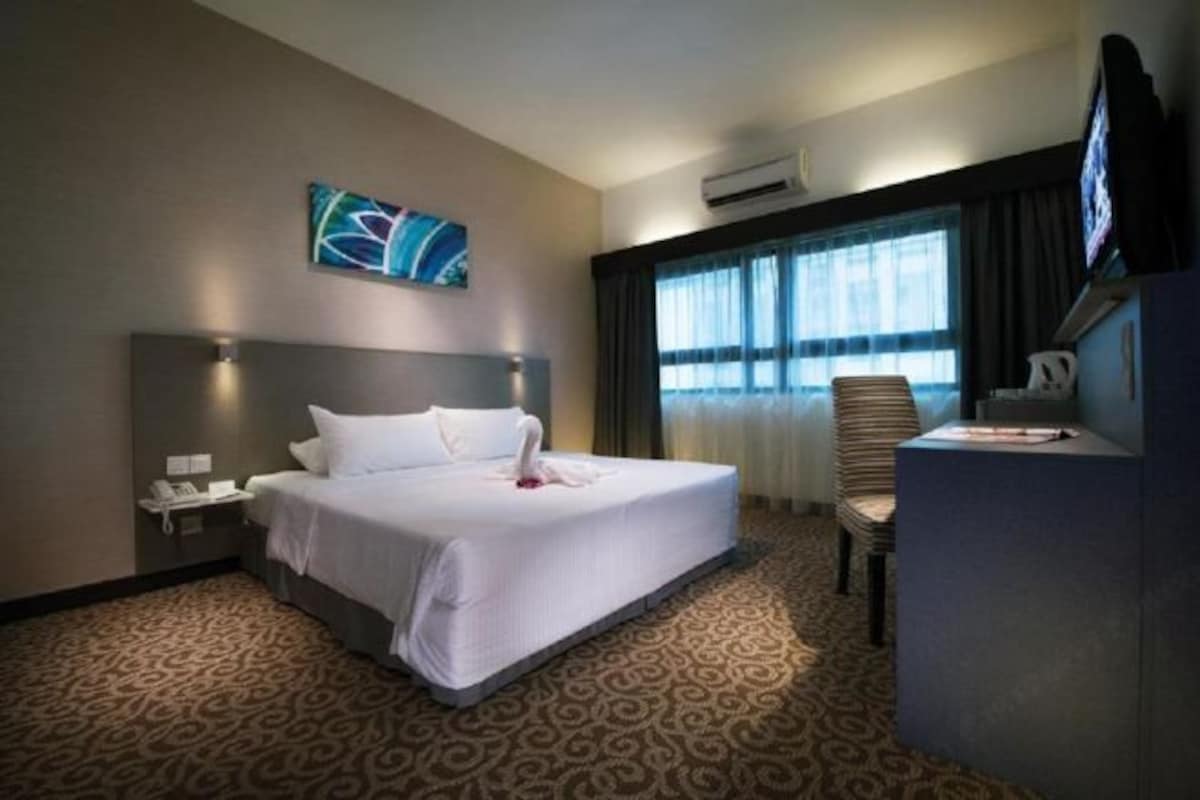 A hotel room with a large bed, a desk, a chair, a TV, and a window with curtains.