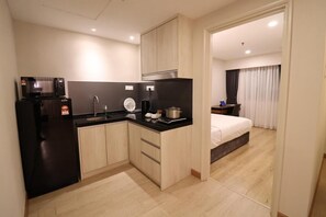Une cuisine compacte équipée d’un four à micro-ondes, d’un évier et de placards, qui donne sur une chambre avec un lit et une petite table.
