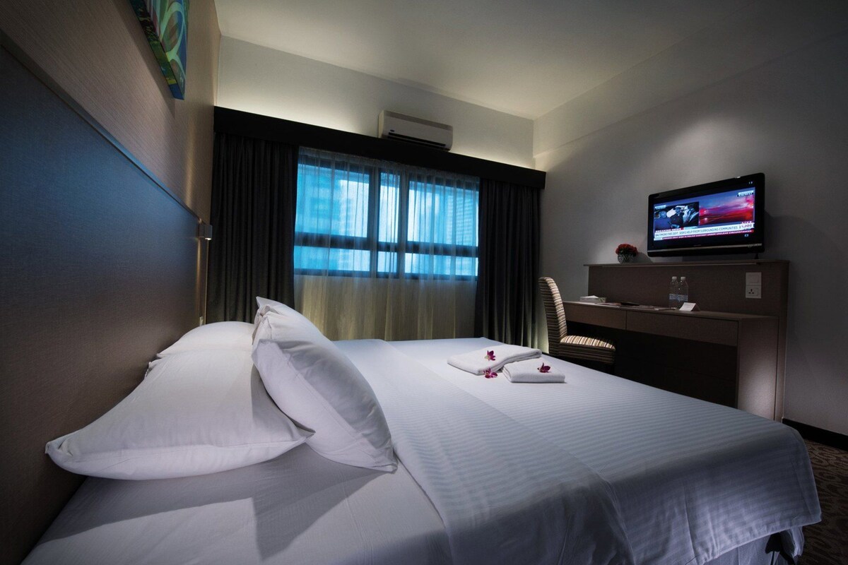 A hotel room with a bed, a desk, a television, and a window with curtains.