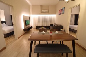A hotel room with a dining table, two couches, a TV, and a bed. - Crown Regency Serviced Suites (Kuala Lumpur)