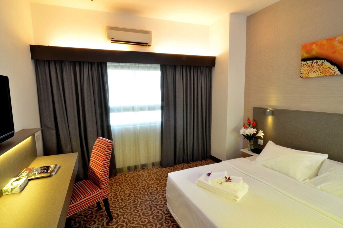 A hotel room with a bed, a desk, a chair, a television, and a window with curtains.