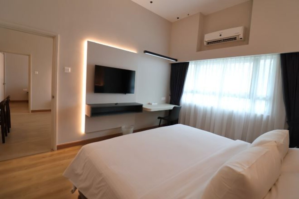 A hotel room with a large bed, a flat-screen TV mounted on the wall, a small desk, and a window with curtains.