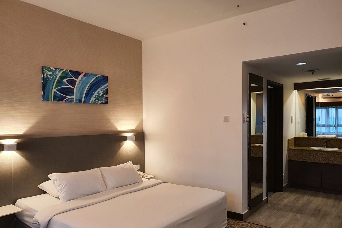 A hotel room with a bed, a nightstand, a painting on the wall, and a bathroom visible through an open door.