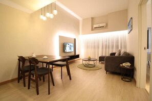 A modern living room with a dining table, chairs, a sofa, a TV, and a small side table. - Crown Regency Serviced Suites (Kuala Lumpur)