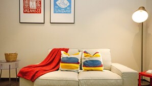 A living room with a sofa, colorful pillows, a red throw blanket, a small side table, and a lamp. - Crown Regency Serviced Suites (Kuala Lumpur)