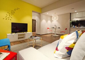 A modern living room with a flat-screen TV, a dining area with a chandelier, and a kitchen area. - Crown Regency Serviced Suites (Kuala Lumpur)