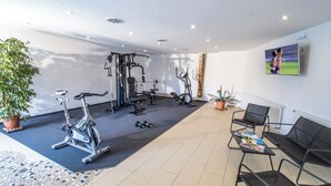 Et fitnessrum med træningsudstyr, fjernsyn og siddeområde.