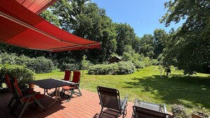 Eine Terrasse mit Tisch und Stühlen, einem Grill und einem roten Sonnensegel.