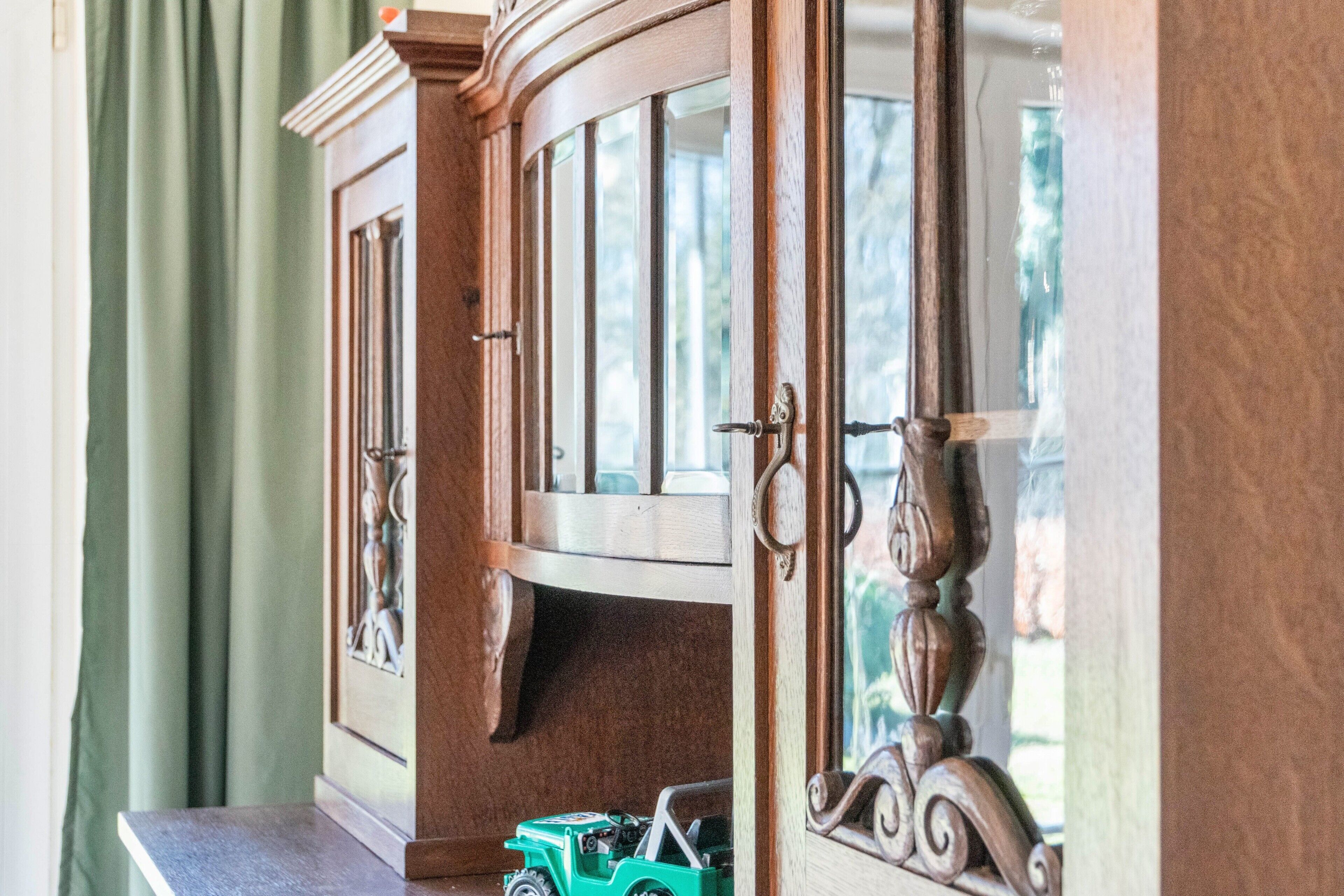 Um armário de madeira com portas de vidro e um carrinho de brinquedo verde dentro.