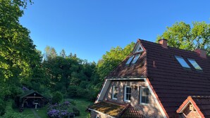 Ein zweistöckiges Backsteinhaus mit geneigtem Dach, einem kleinen angebauten Schuppen und einem gepflegten Garten mit einem Weg.