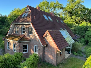 A two-story house with a sloped roof, a visible chimney, and a small attached structure with a window. - Holiday Home 'Friesenwald' with Private Terrace, Shared Garden, and Wi-Fi (Zetel)