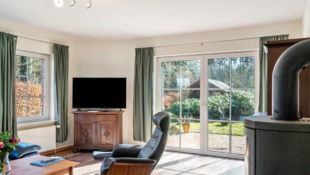 Ein modernes Wohnzimmer mit einem Flachbildfernseher, einem Ledersessel, einem Holzkabinett und einer großen Glasschiebetür, die zu einem Außenbereich führt.