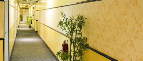 Un pasillo con paredes amarillas, un papel tapiz estampado y un extintor montado en la pared.