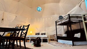 Una habitació tipus tenda acollidora amb un llit superposat, una taula, cadires i una petita finestra.