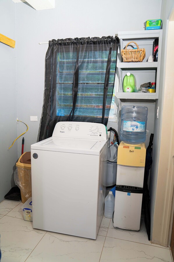 A laundry room with a front-loading washer and dryer, a water dispenser, and a shelf with cleaning supplies.