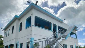 A two-story building with a staircase leading to the upper floor, surrounded by a landscaped garden. - Chenko Villas & Cars (Jennings)