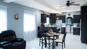A modern kitchen with dark cabinetry, a dining area with a table and chairs, and a ceiling fan. - Chenko Villas & Cars (Jennings)